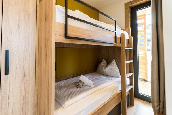 A bunk bed with a wooden frame, a lower bunk with pillows, and a window with curtains.