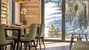 Un espace repas avec une table et des chaises en bois, un luminaire suspendu et une vue sur un paysage enneigé par de grandes fenêtres.