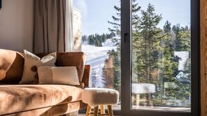 A modern living room with a large window, a brown sofa, and a wooden stool. - Alpin Peaks (Stadl-Predlitz)