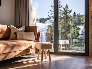 Ett modernt vardagsrum med ett stort fönster, en brun soffa och en träpall.