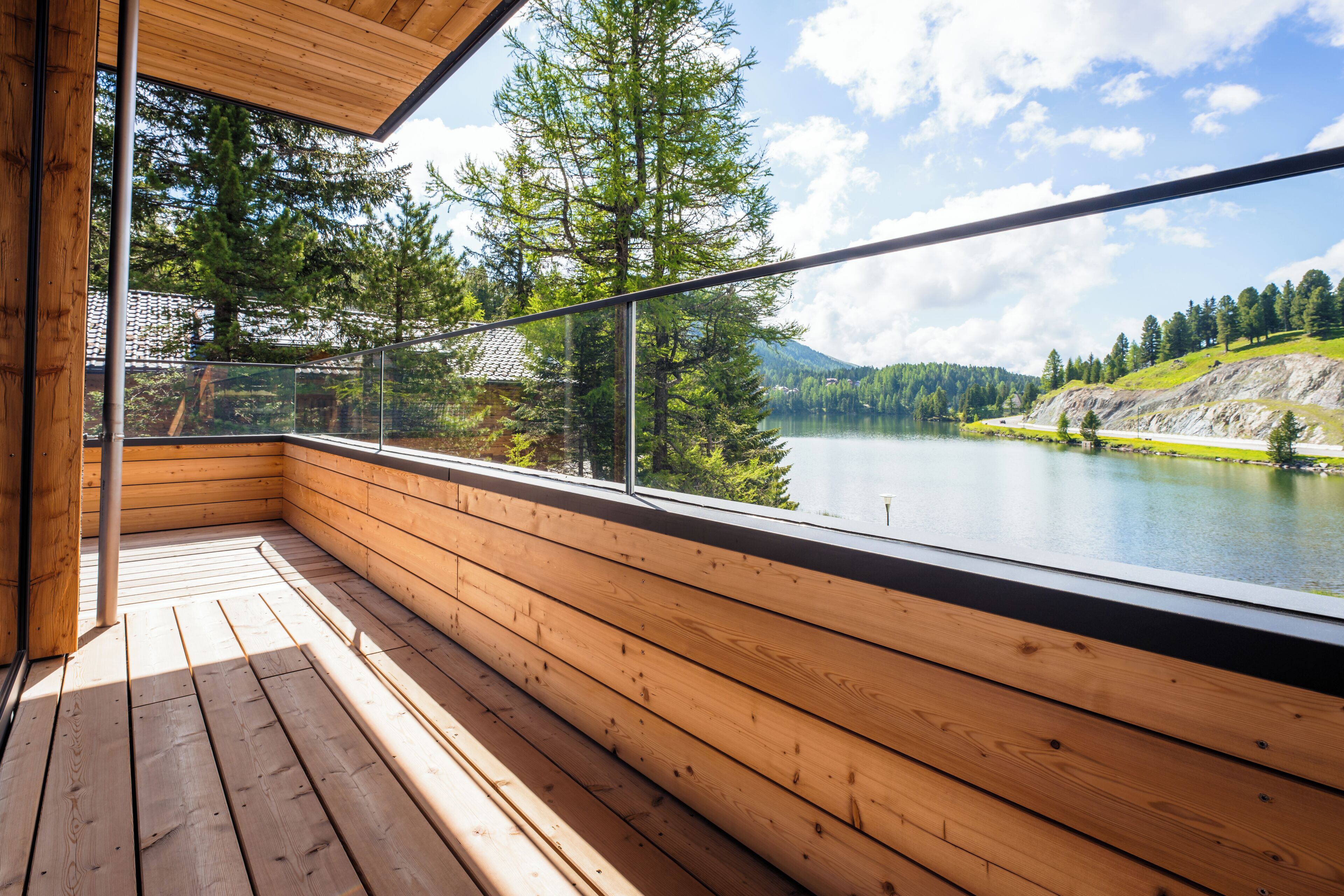 Eine Holzterrasse mit Glastrennwand mit Blick auf einen See und einen Wald.