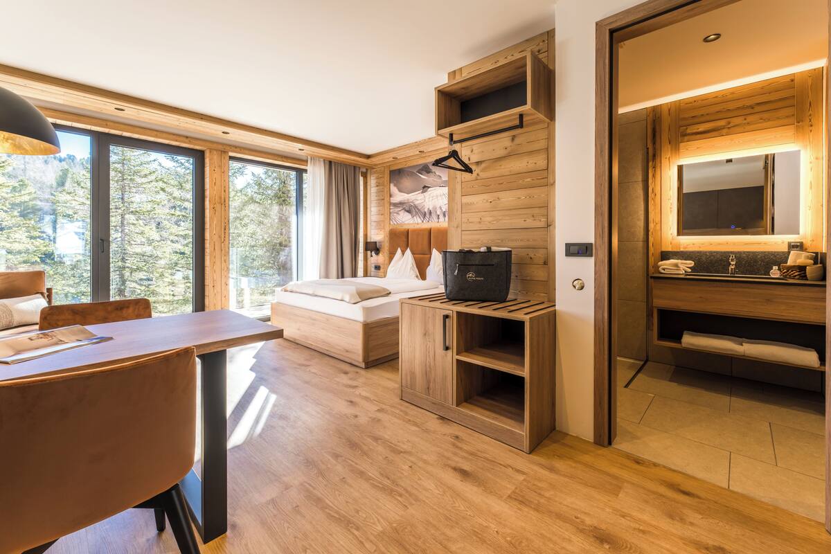 A modern room with a bed, a wooden cabinet, a desk, and a bathroom with a mirror and sink.