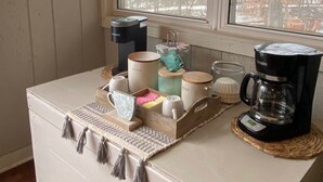 Een keuken met een koffiezetapparaat, suiker-en roomvoorraad en een plank met mokken.