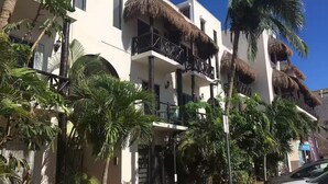 Un hôtel à plusieurs étages doté de balcons, de palmiers et d’un chemin bordé de briques rouges.