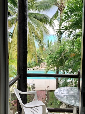 A balcony with a view of a swimming pool, surrounded by palm trees and greenery. - Beautiful condo by the beach (Playa del Carmen)