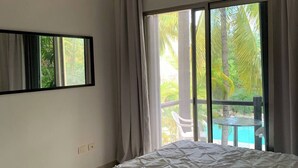 Une chambre dotée d’un grand lit, d’un ventilateur de plafond, d’une fenêtre avec des rideaux et offrant une vue sur une piscine et des palmiers.