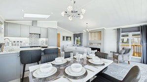 A modern kitchen with grey cabinets, a dining area with a white table set for six, and a living area with a grey sofa and a balcony. - Host & Stay | Marble Lodge (Beverley)
