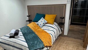 Un dormitorio moderno con tragaluz, una cama con ropa de cama a rayas, cabecera de madera y alfombra tejida.