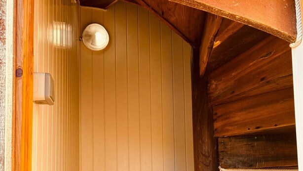 Eine Holztreppe führt zu einem Raum mit weißen Wänden und einer Deckenleuchte.