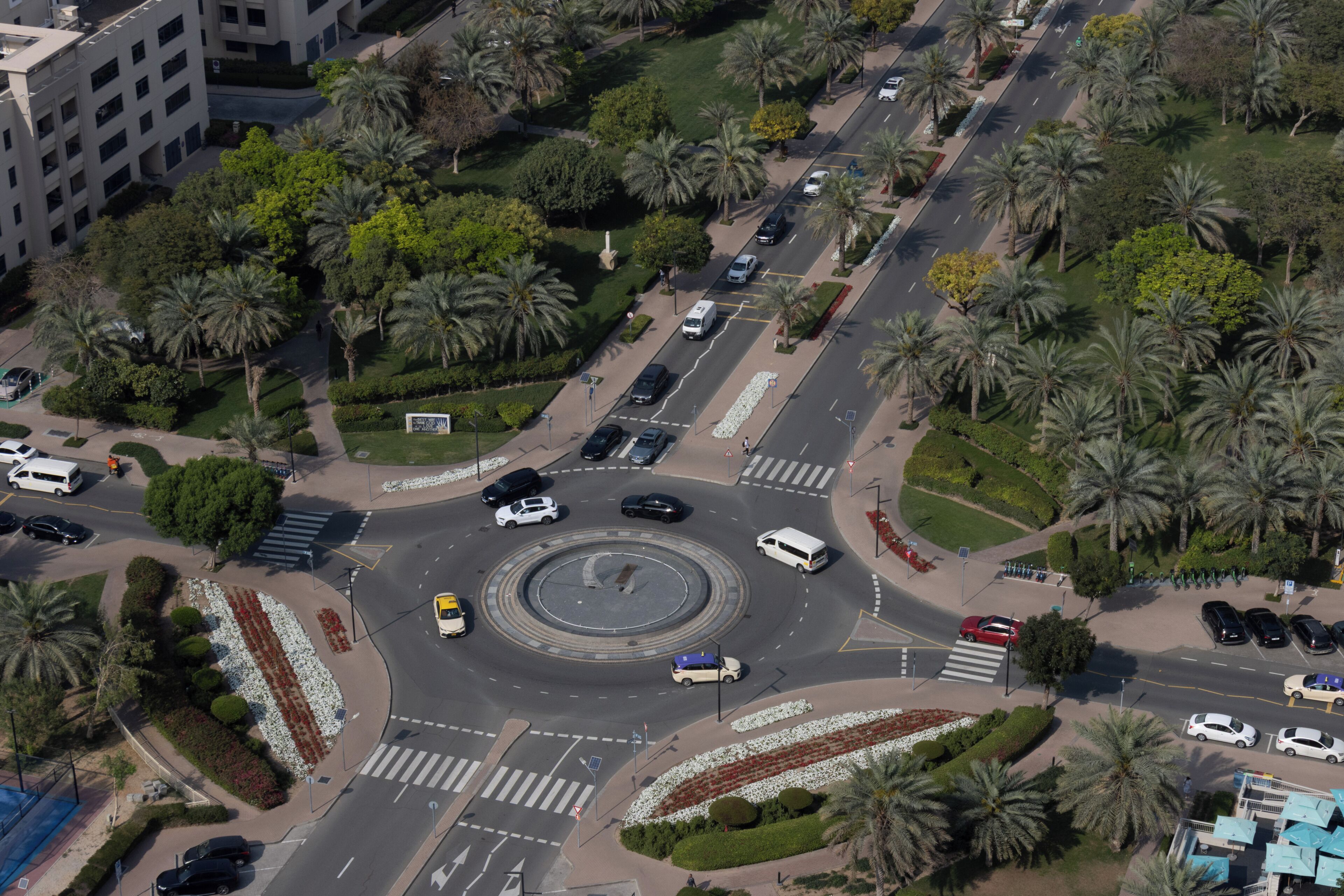 Vue aérienne d’un rond-point agrémenté de palmiers, avec un îlot central et des bâtiments environnants.