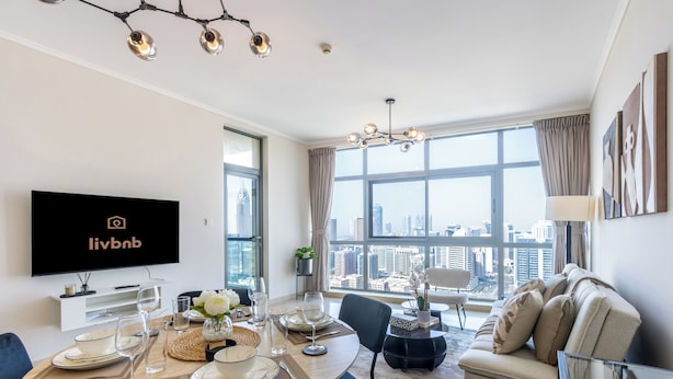 Un salón moderno con comedor, ventanas amplias, televisor de pantalla plana y vista a la ciudad.