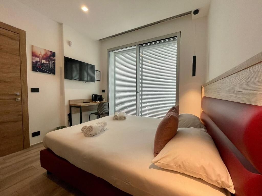 Une chambre à coucher avec un lit, un bureau, une chaise, une télévision et une fenêtre avec des stores.