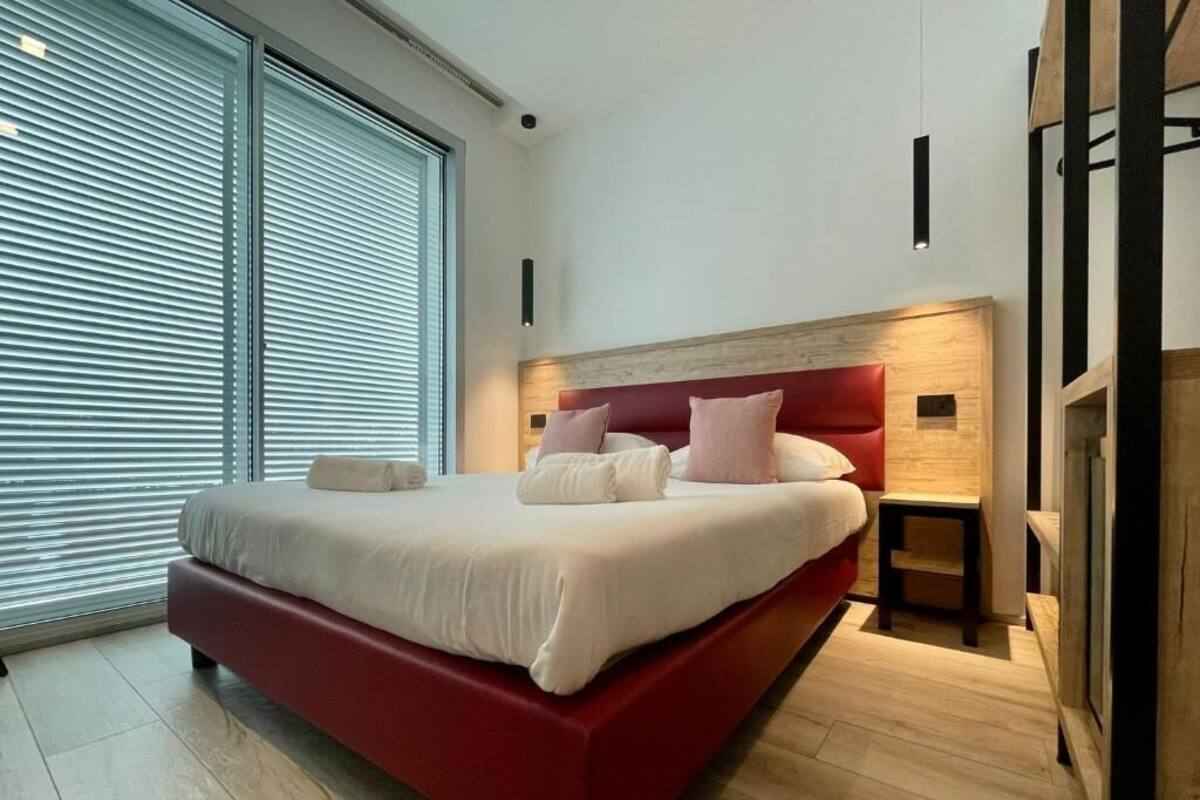 Un dormitorio moderno con una cama roja, ropa de cama blanca y un cabecero de madera.