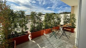 Μια ταράτσα με γλάστρες γεμάτες φυτά, ένα ξύλινο τραπέζι και καρέκλες.