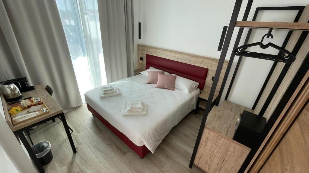 Habitación de hotel con cama, escritorio, silla, perchero y ventana con cortinas.