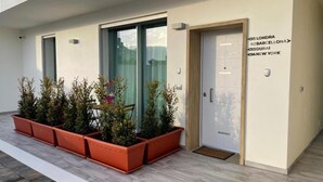 Ένα σύγχρονο κτίριο με γυάλινη πόρτα, φυτά σε γλάστρες και μια επιγραφή στον τοίχο με ονόματα πόλεων.
