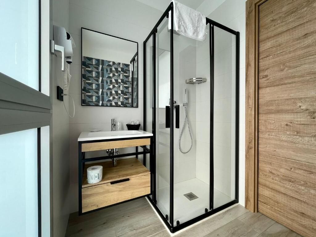 Ein modernes Badezimmer mit einer gläsernen Duschkabine, einem Holzkosmetikschrank und einem großen Spiegel.