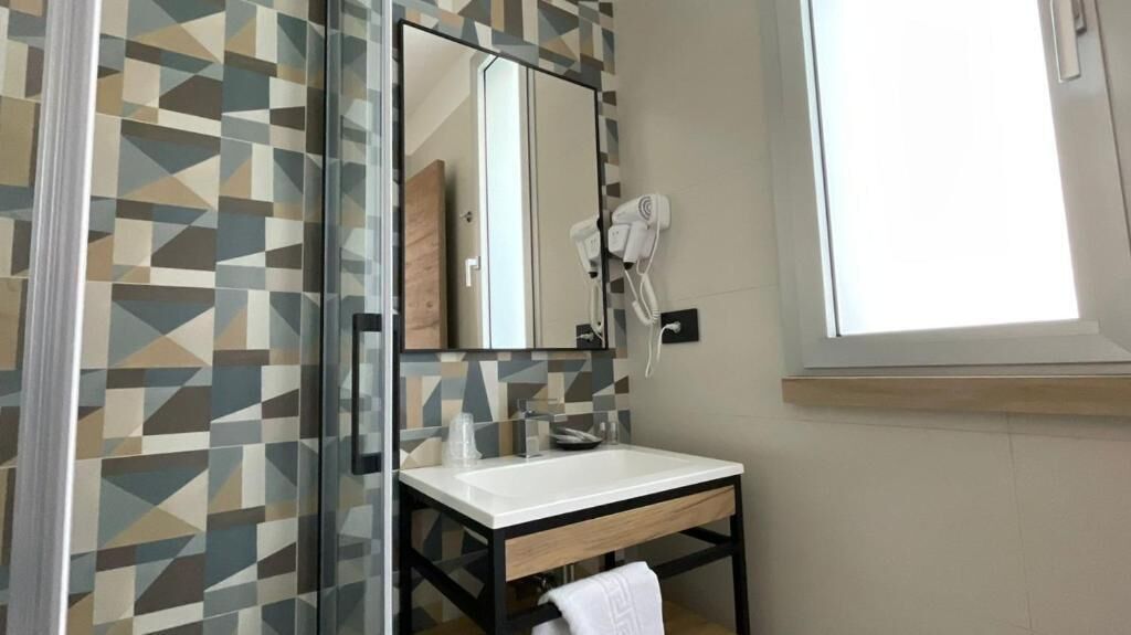 A bathroom with a geometric patterned wall, a mirror, a sink, a towel, and a hairdryer.