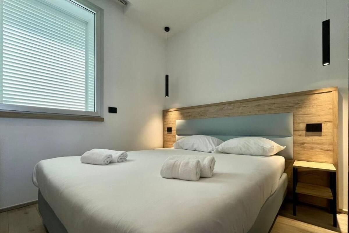 Un dormitorio moderno con una cama grande, cabecera de madera, mesitas de noche y una ventana con persianas.