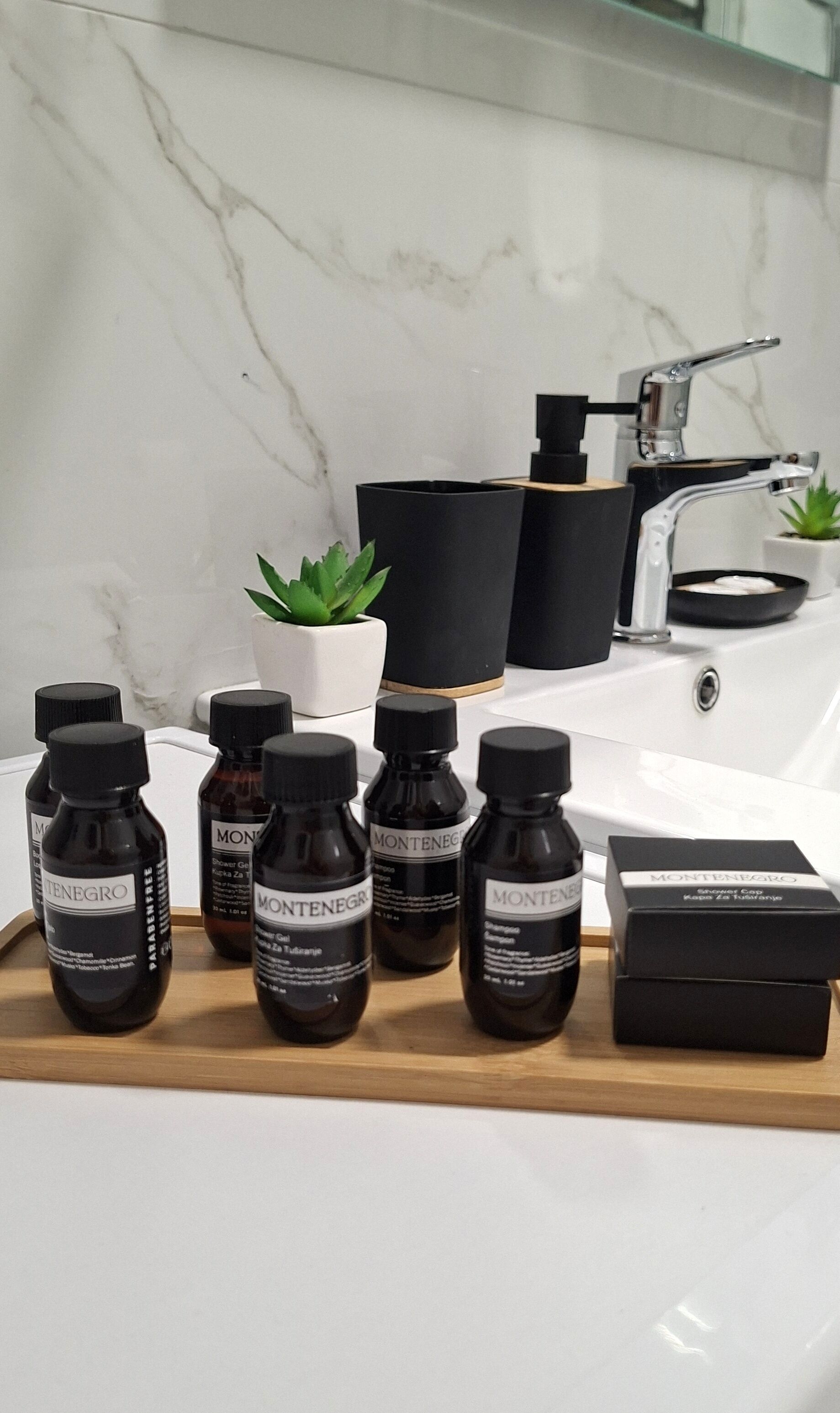 Un bagno con un lavandino bianco, una pianta in vaso e diverse bottiglie di bagnoschiuma Montenegro.