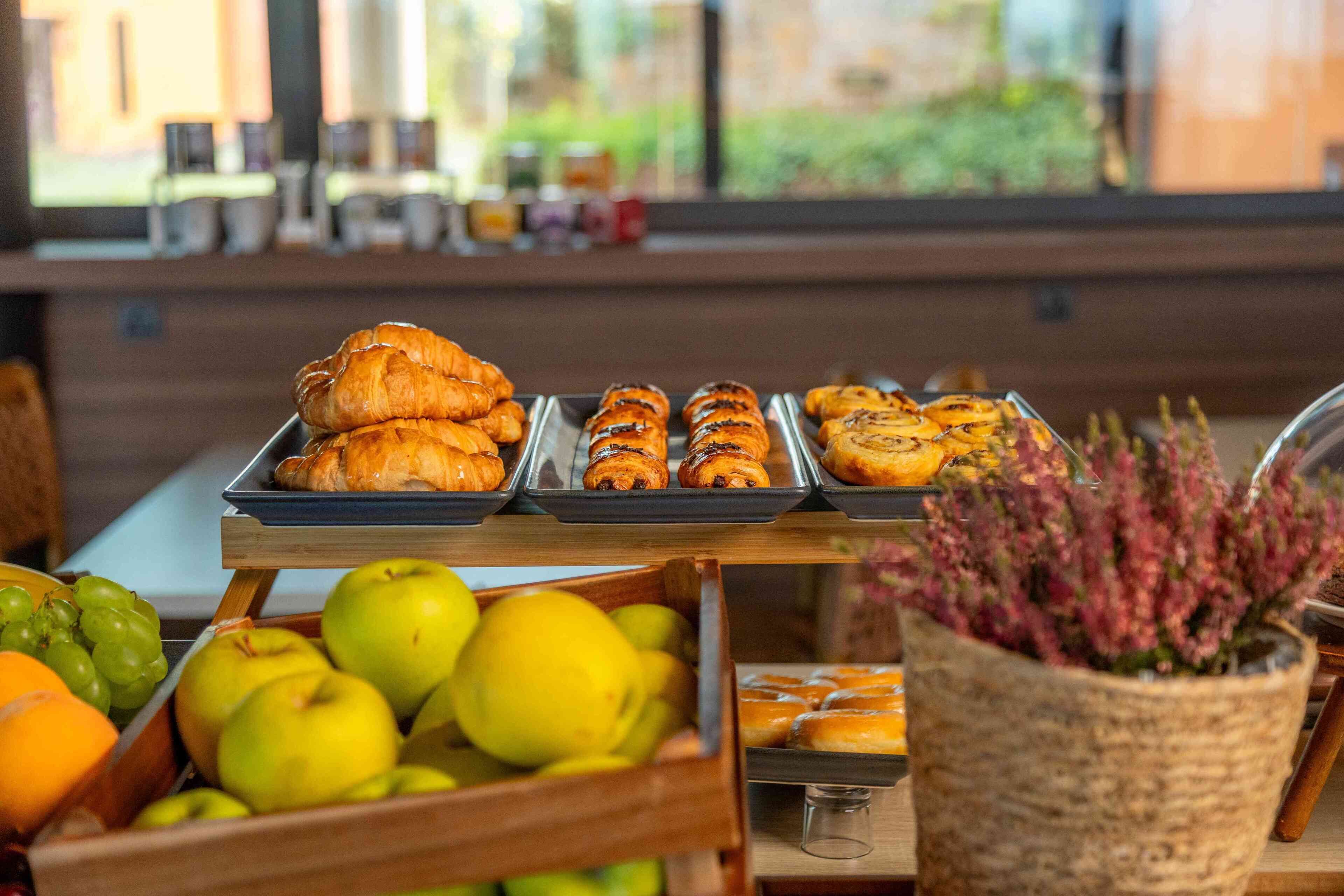 A breakfast buffet with pastries, fruits, and a potted plant.