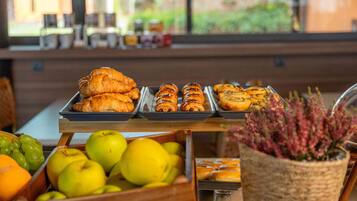 A breakfast buffet with pastries, fruits, and a potted plant.