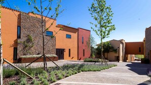 A courtyard with buildings featuring stone and stucco exteriors, a gravel path, and young trees. - El Vilar de la Duquessa (Cardona)