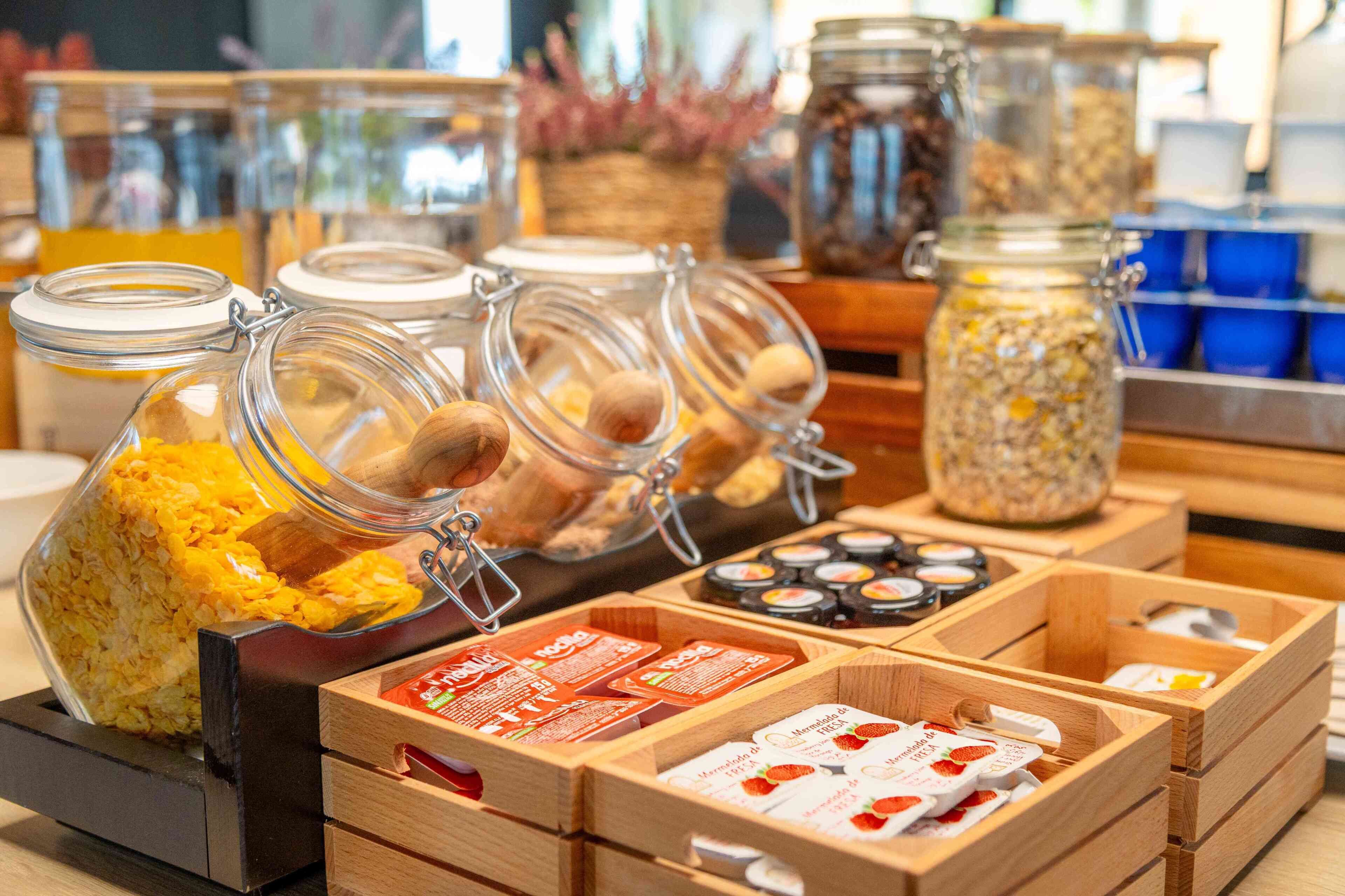 A breakfast buffet with various food items and condiments in glass jars and wooden boxes.