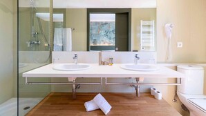 A modern bathroom with two sinks, a glass shower enclosure, a towel on the floor, and a hairdryer on the wall. - El Vilar de la Duquessa (Cardona)