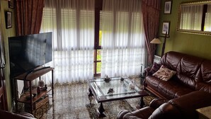 Un salon avec un canapé en cuir marron, une table basse en verre, un téléviseur et des rideaux, avec un luminaire placé au-dessus.