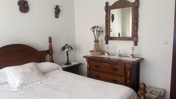 A bedroom with a wooden bed, a nightstand with a lamp, a dresser, a mirror, and a vase with flowers.