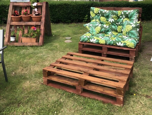 A wooden bench and a sofa with a tropical leaf pattern, both placed on a grassy lawn. - Welcome to Villa Neli Playa (Foz)