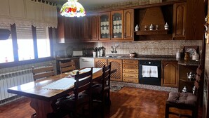 Une cuisine avec des meubles de rangement en bois, une table à manger avec des chaises, un luminaire suspendu et une fenêtre avec des rideaux.