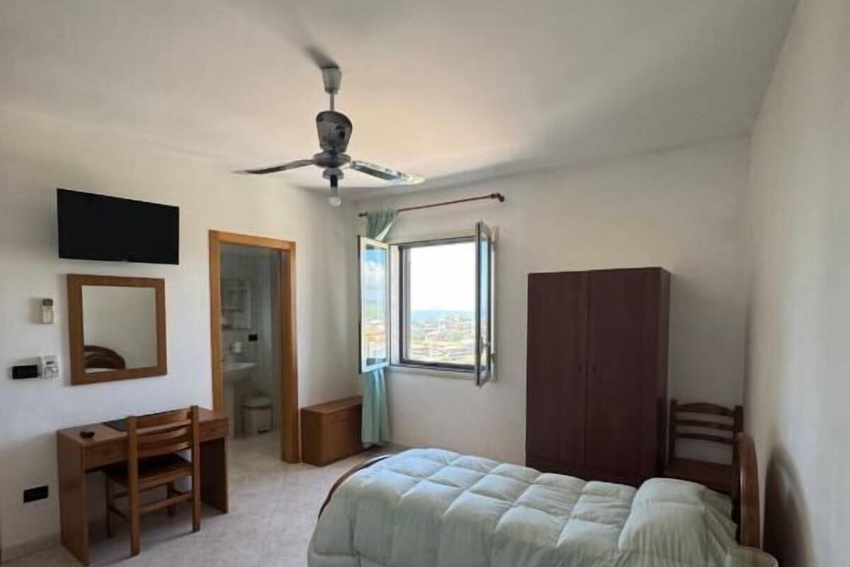 Une chambre avec deux lits, un bureau, une armoire, un ventilateur de plafond et une fenêtre donnant sur un beau paysage.