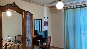 A bedroom with a bed, a desk, a chair, a wardrobe, a ceiling fan, and a window with curtains. - bed and breakfast della palma (Gela)