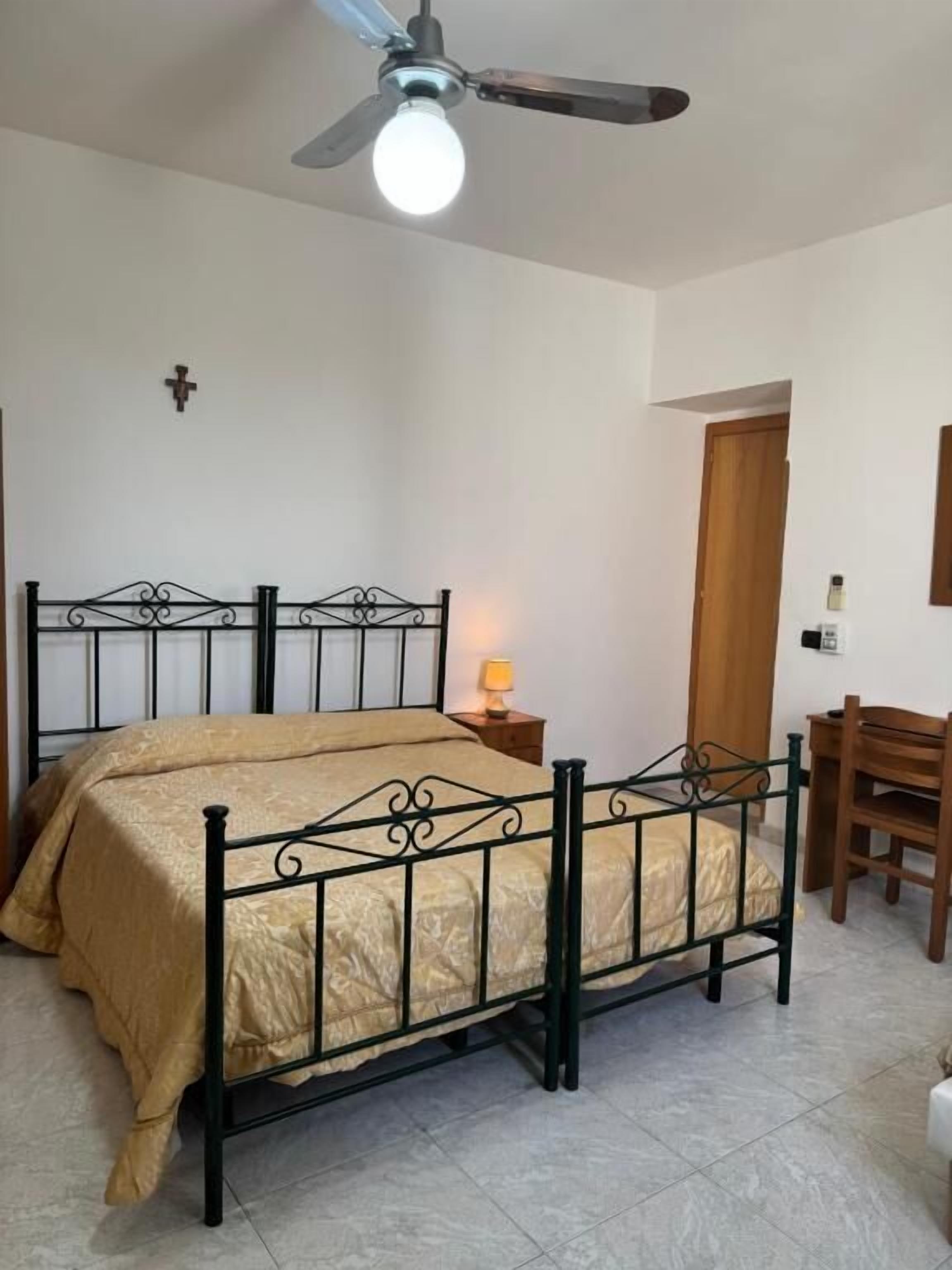 Ein Schlafzimmer mit Bett, Schreibtisch, Stuhl, Deckenventilator und Nachttisch mit Lampe.