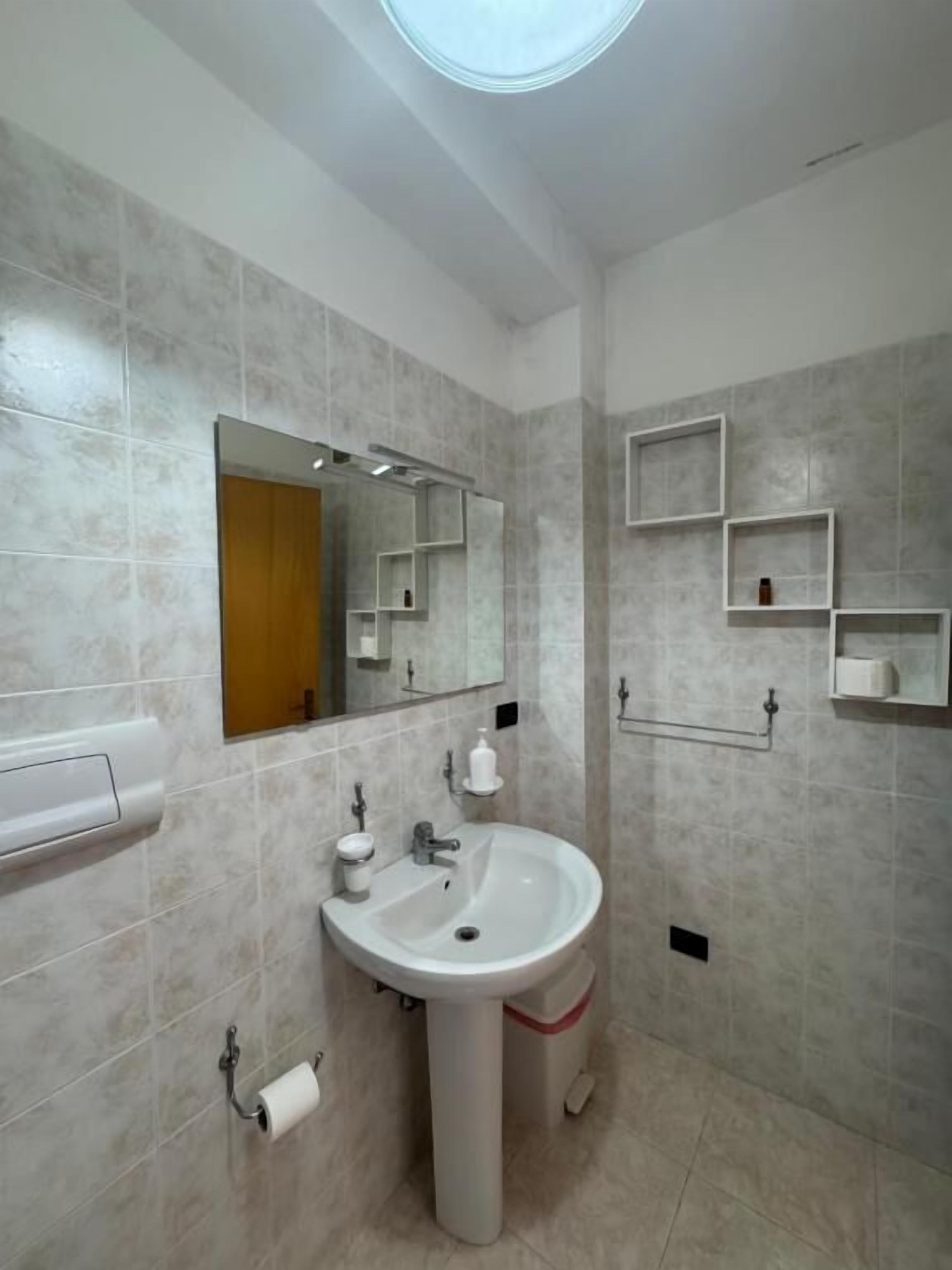 A modern bathroom with a pedestal sink, a mirror, and built-in shelves.