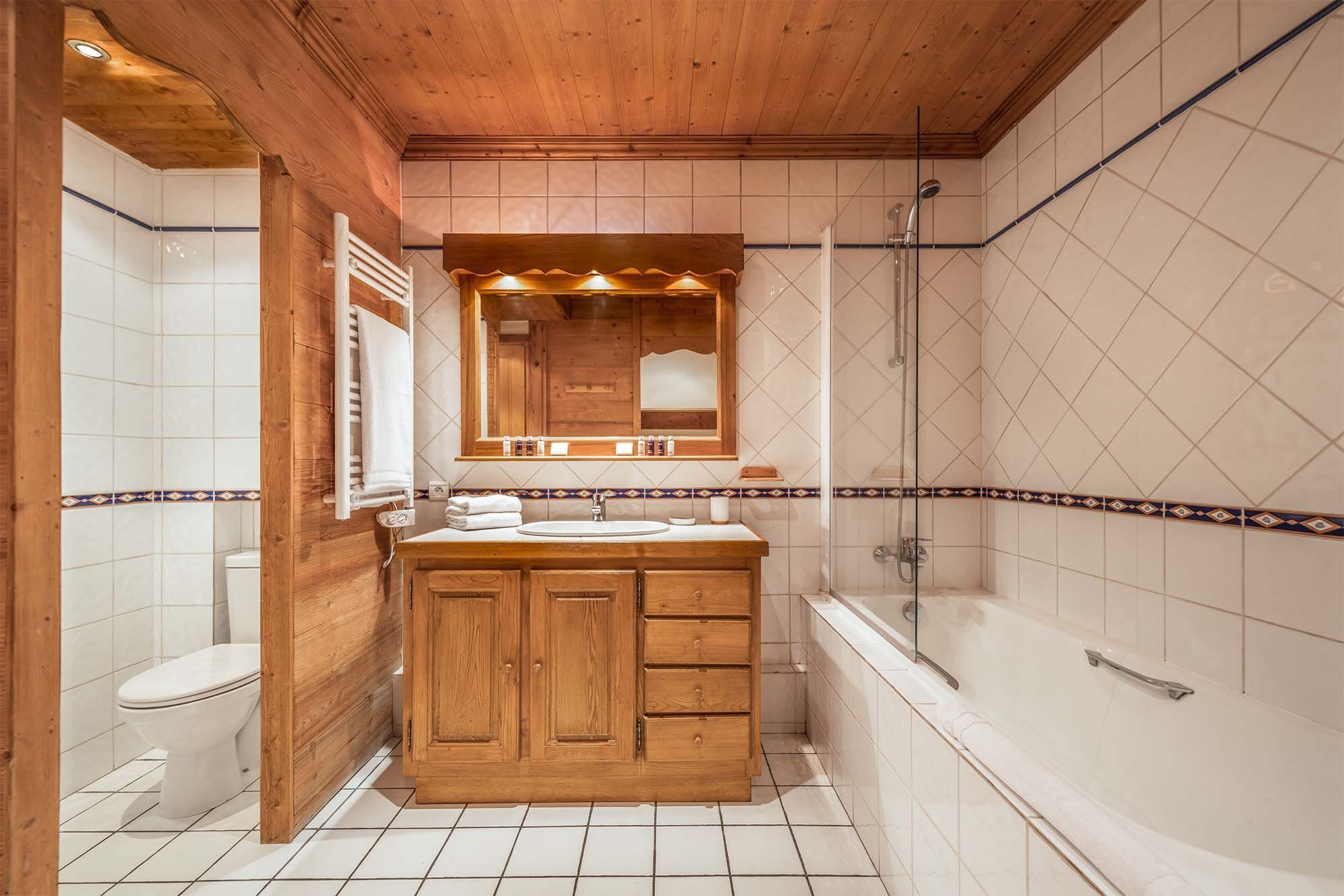 A bathroom with a wooden vanity, a mirror, a shower, and tiled walls.