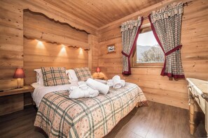 A wooden cabin bedroom with a bed, two bedside lamps, a window with curtains, and a wooden dresser.