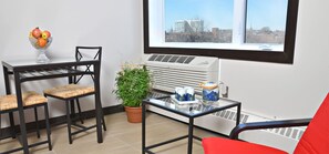 Une pièce comprenant une table, des chaises, une plante en pot, une fenêtre donnant sur la ville et un appareil de climatisation.