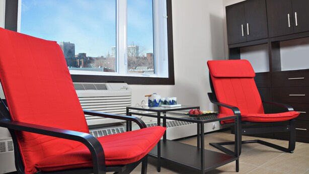 A modern kitchen with two red chairs, a small table, and a window with a city view. - Cjour loft Apartment (Montréal)