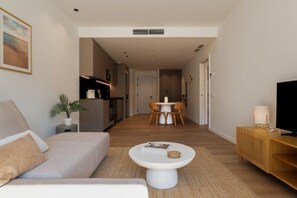 Ein modernes Wohnzimmer mit einer Couch, einem Couchtisch, einer TV-Konsole und einem Essbereich im Hintergrund.