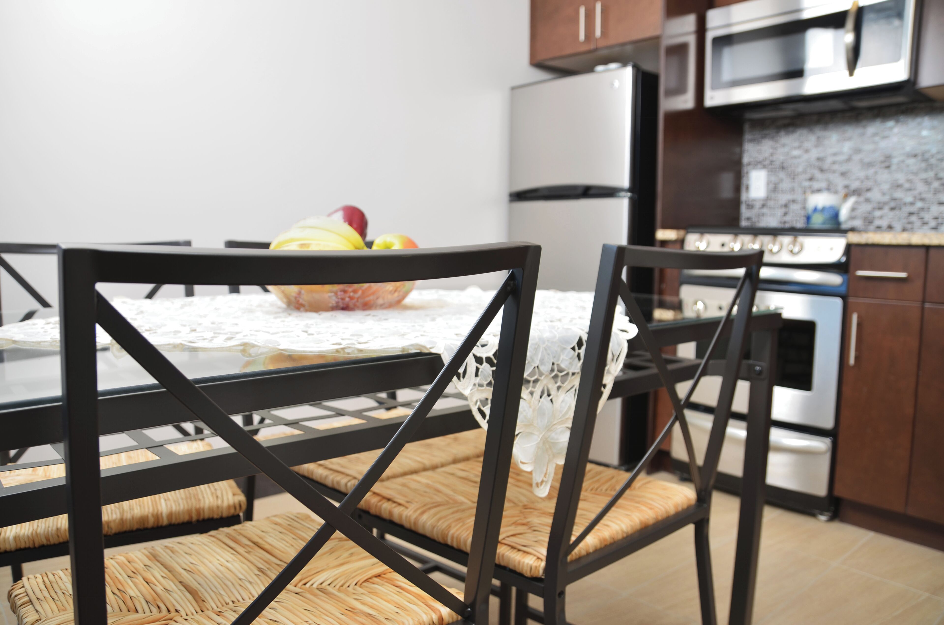 A kitchen with a dining table, chairs, a fruit bowl, and modern appliances.