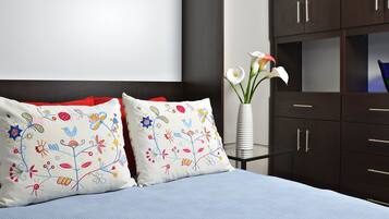 A bed with two decorative pillows, a vase with flowers, and a dark wooden dresser with drawers.