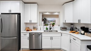 A modern kitchen with white cabinets, stainless steel appliances, a dishwasher, and a view of the outdoors. - Sip & Swim | Heated Pool • Hot Tub • Games (Tucson)