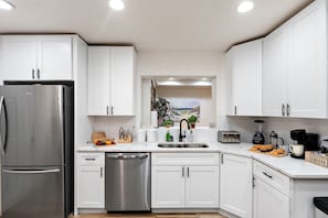Una cocina moderna con gabinetes blancos, electrodomésticos de acero inoxidable, lavavajillas y vistas al exterior.
