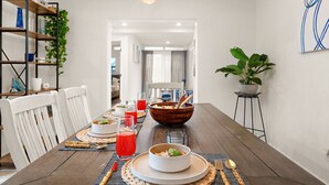A dining area with a wooden table, white chairs, a large bowl, and a hanging light fixture. - Sip & Swim | Heated Pool • Hot Tub • Games (Tucson)