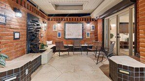 An outdoor patio with brick walls, a tiled floor, and a table with chairs. - Sip & Swim | Heated Pool • Hot Tub • Games (Tucson)