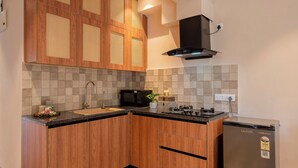 A kitchen with wooden cabinets, a stainless steel refrigerator, a microwave, and a sink. - Staymaster Solintra 2BHK C402 (Verem)