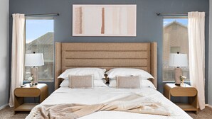 A bedroom with a large bed, two bedside tables, a headboard, and a window with curtains.